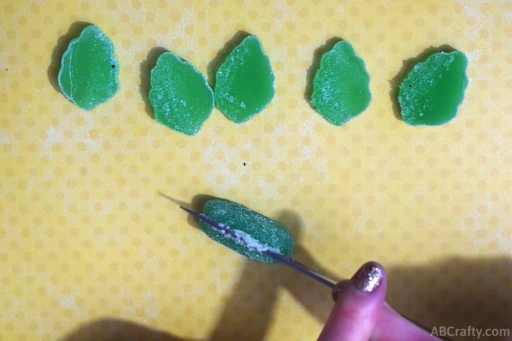 cutting a mint green leaf gummy into thirds with other gummies above it already cut