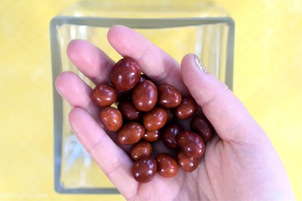 holding a handful of candy boston baked beans over a clear square glass container