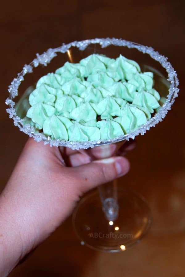 hand holding a martini glass with sugar on the rim and green bailey's buttercream frosting on a cupcake inside the martini glass