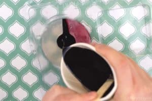 pouring melted black glycerin soap into the center of a pokeball shape in a plastic round soap mold