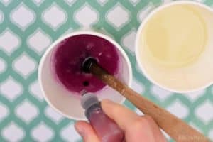 dropping red soap dye into a paper cup with melted glycerin soap that is already slightly red