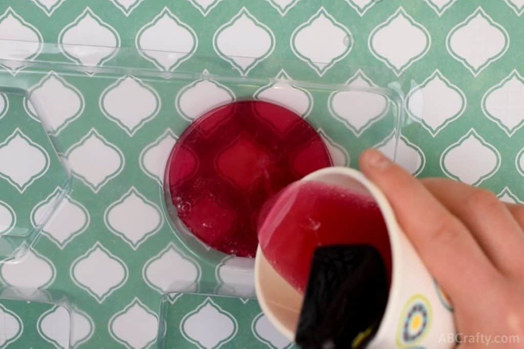 pouring melted red clear soap into a round soap mold