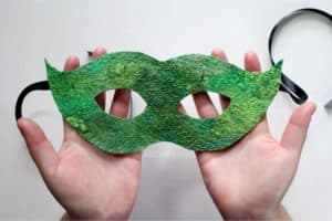 holding a finished green masquerade mask made out of wet felted handmade felt with black satin ribbon hanging from the sides