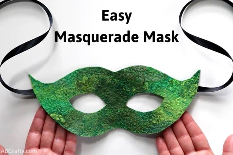hands holding a green masquerade mask made out of handmade felt with black ribbon hanging from the sides with the title "easy masquerade mask"