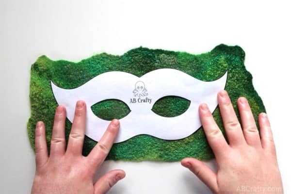 placing ab crafty masquerade mask template over green handmade felt