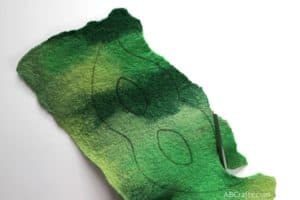 cutting out a piece of green handmade felt that has the outline of a mask transferred using a sulky transfer pen