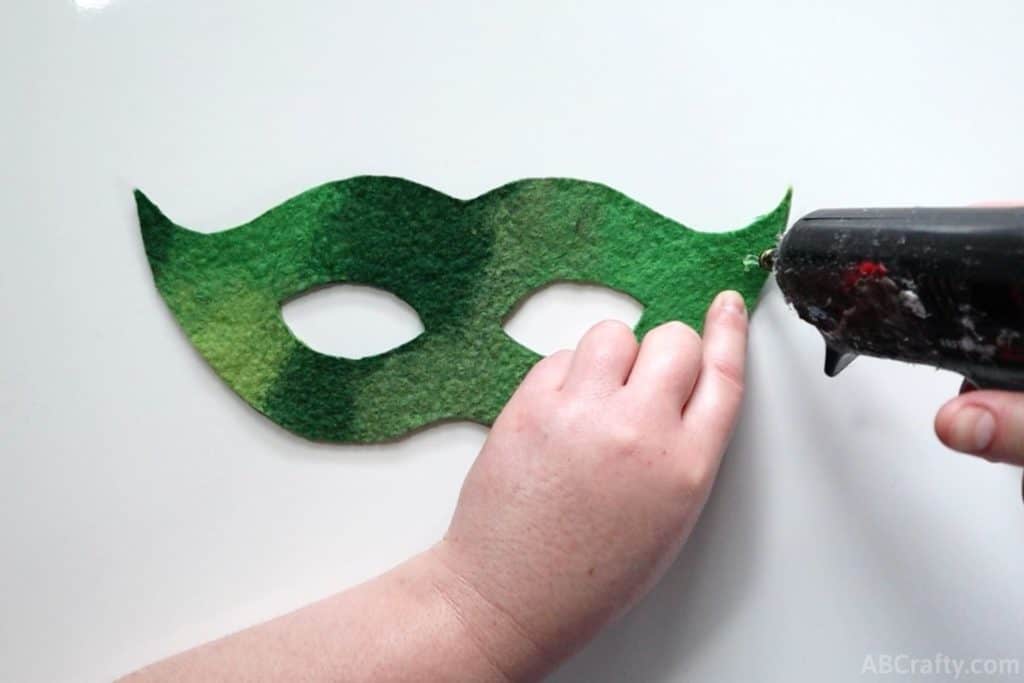 using a glue gun to put glue onto the edge of a green mask