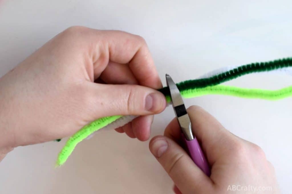 using purple wire cutters to cut a dark green, light green, and white pipe cleaner or chenille stem