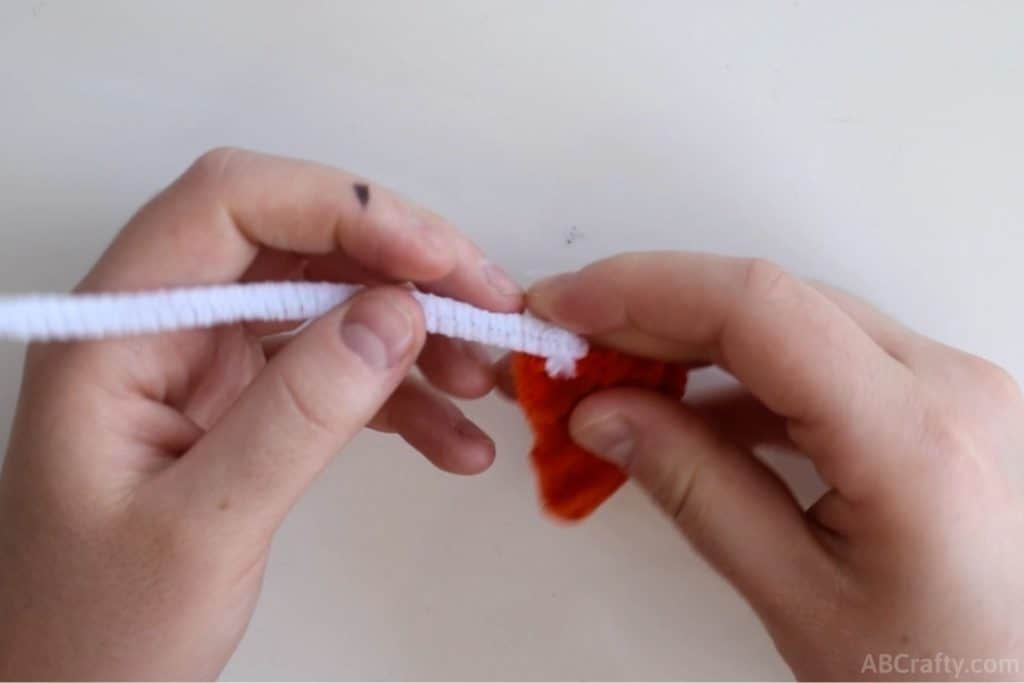 attaching a white pipe cleaner to a triangle made from an orange pipe cleaner