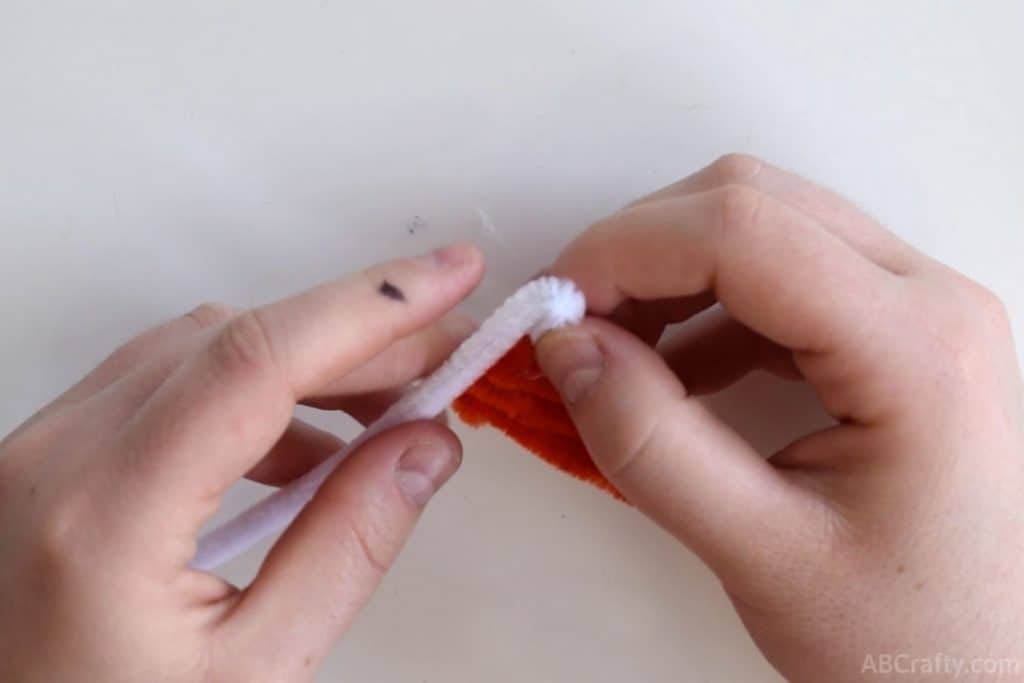 bending a white pipe cleaner over that is attached to a triangle of orange pipe cleaner