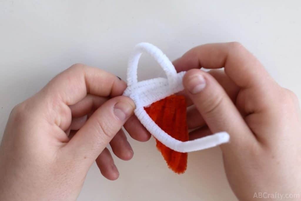 forming the loop of a scoop of ice cream using a white pipe cleaner on top of a cone made of orange pipe cleaner