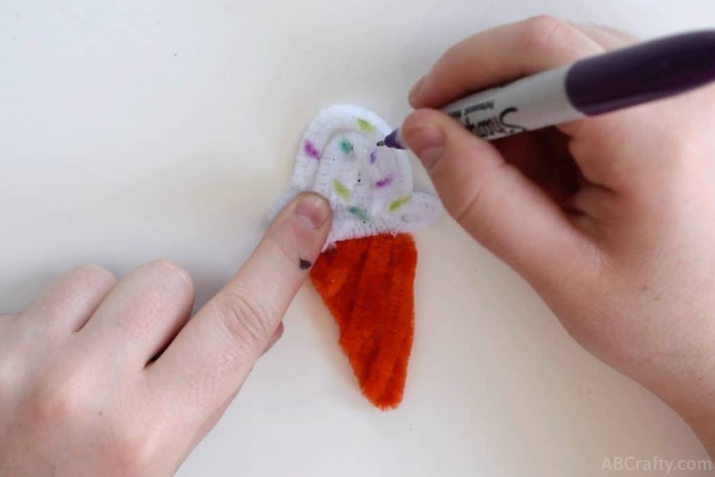 using a purple sharpie to draw sprinkles onto an ice cream cone made of pipe cleaners