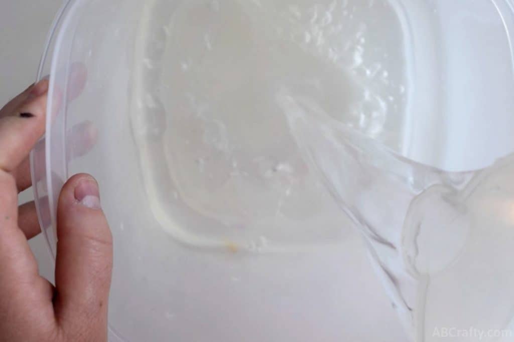 pouring water from a measuring cup into a plastic container