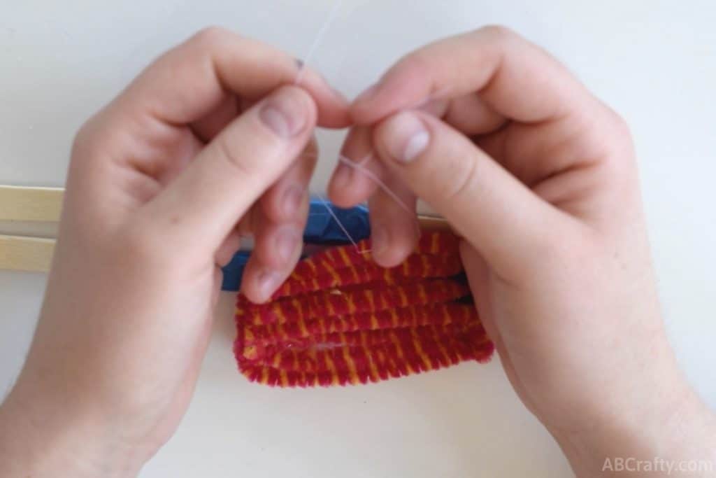 tying white thread into a knot on top of the pipe cleaner popsicle