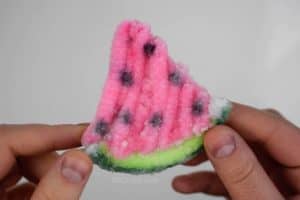 holding a watermelon slice covered in borax crystals made of pipe cleaners