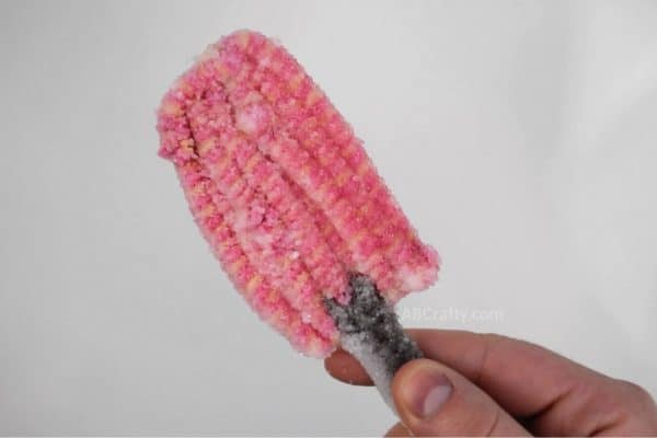 holding a pink and orange striped popsicle covered in crystals made from borax