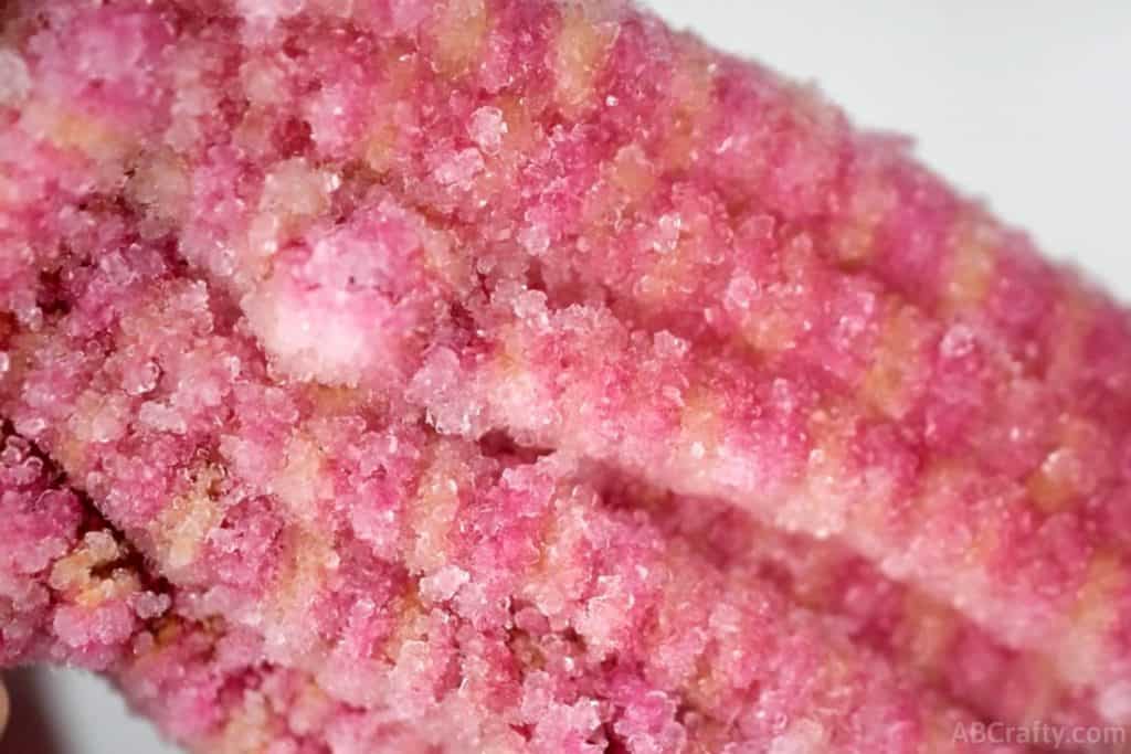 close up photo of borax crystals formed on a pink and orange striped pipecleaner