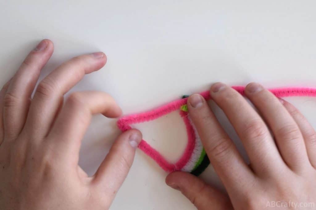 folding a pink pipe cleaner or chenille stem into the shape of a triangle to form the outline of a watermelon slice