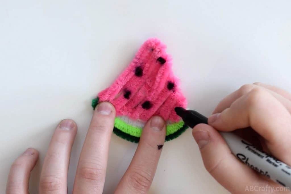 using a black sharpie to draw seeds onto a watermelon made of pipe cleaners
