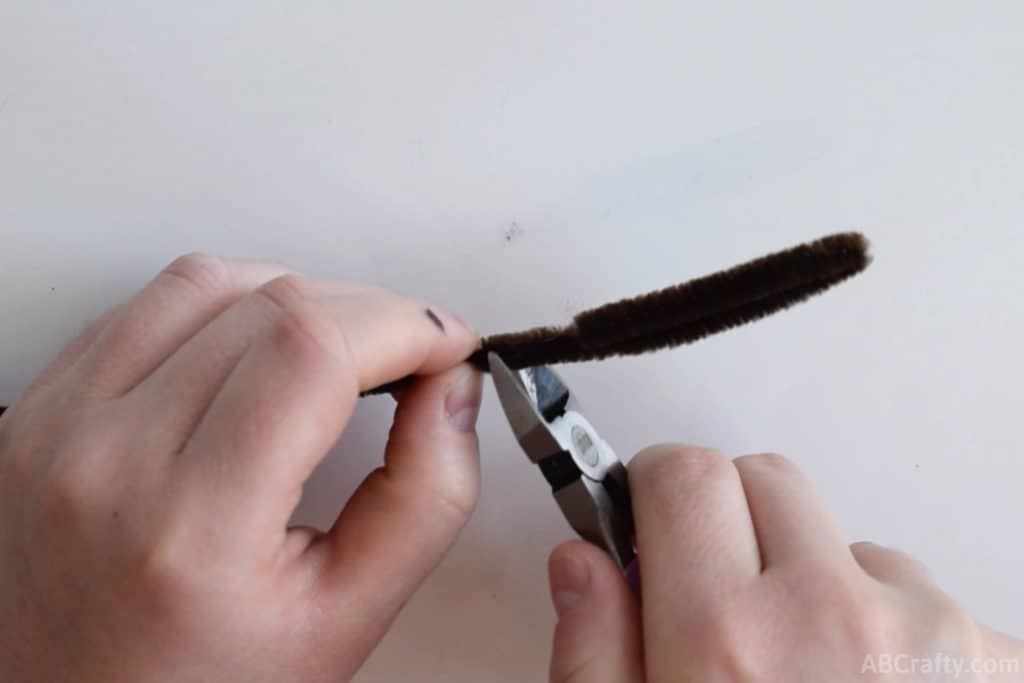 using wire cutters to cut the end of a brown pipe cleaner or chenille stem that has been folded in half
