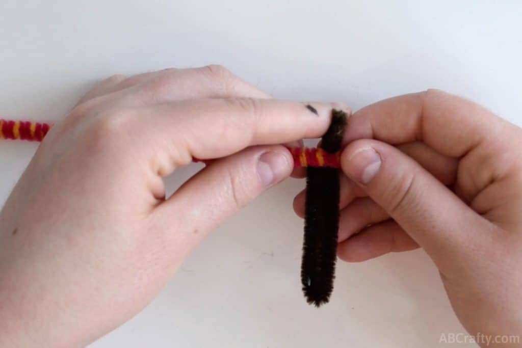 placing a multi colored pipe cleaner or chenille stem over a brown pipe cleaner that has been folded in half with one end sticking further out