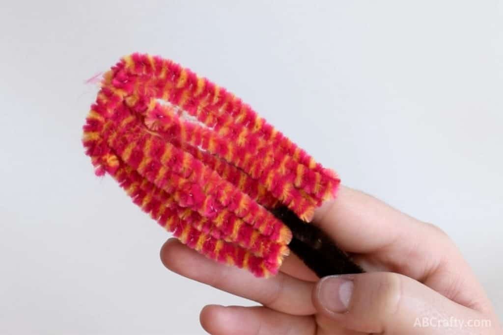 holding a finished popsicle made from a pink and orange striped pipe cleaner