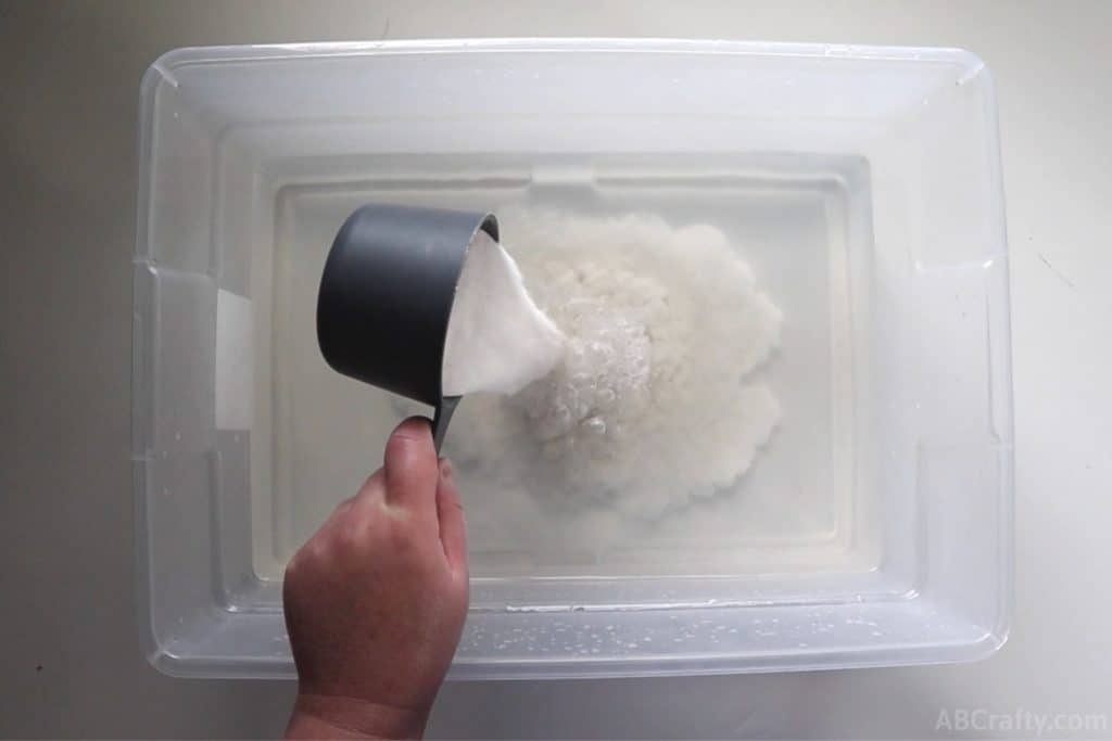 pouring soda ash into a clear plastic tub of water