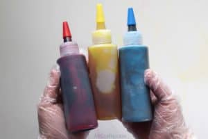 holding bottles of red, yellow, and blue tie dye