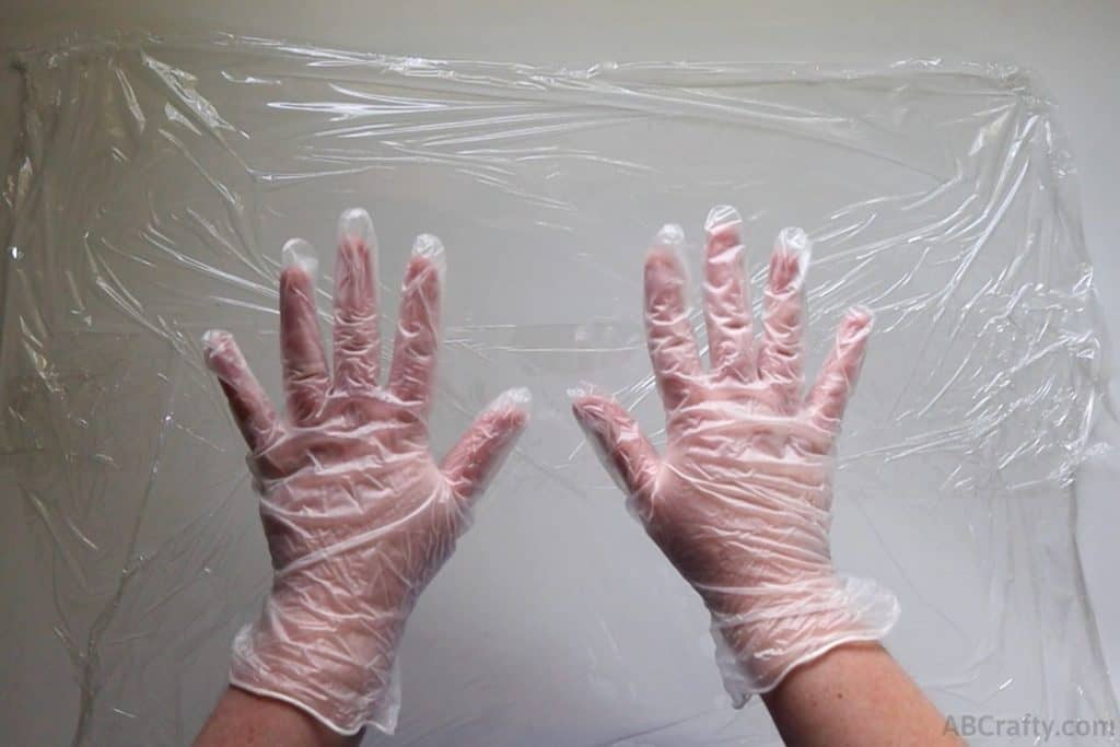 hands wearing vinyl gloves over a table with plastic wrap on it