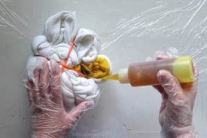 pouring yellow tie dye onto a section of a white sweatshirt in the shape of a spiral wrapped in rubber bands