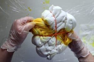pulling apart the layers of a white sweatshirt that's been wrapped into a spiral and wrapped in rubber bands with two opposite sections covered in yellow tie dye