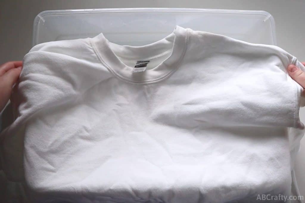 holding a plain white cotton sweatshirt over a plastic tub