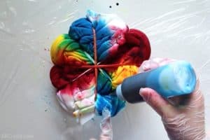 pouring blue tie dye onto a sweatshirt wrapped into a spiral with different primary colors on each section