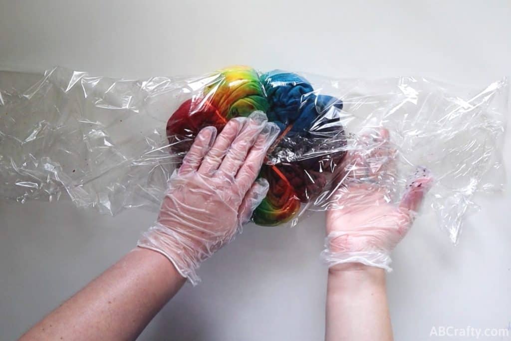 wrapping a rainbow tie dye sweatshirt in plastic wrap while wearing plastic gloves
