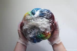 holding a wet sweatshirt covered in rainbow tie dye completely wrapped in plastic wrap