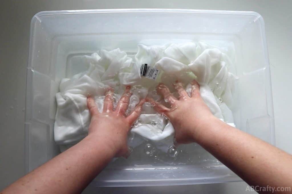 pushing a white sweatshirt into a tub of water