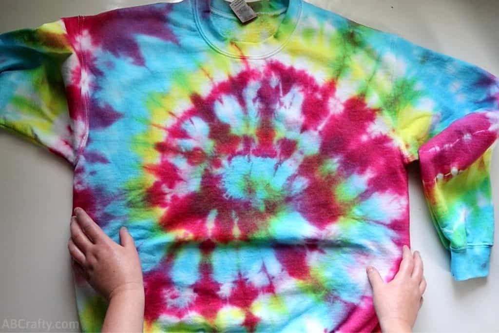 touching a rainbow tie dye sweatshirt on a table with a spiral tie dye pattern