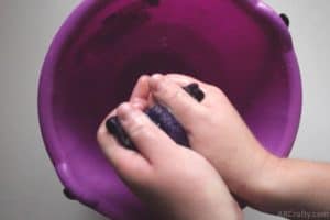 squeezing wet handmade purple fabric over a purple bucket