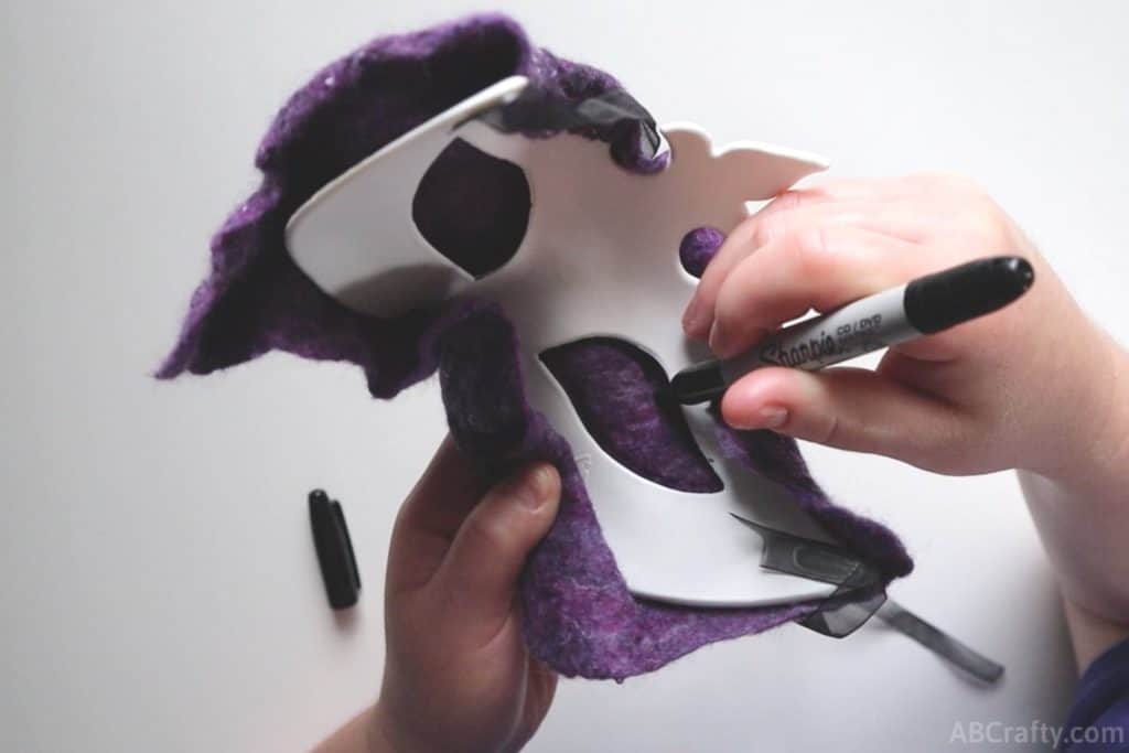 using a permanent black marker to draw the eye holes onto the felted wool using a plastic masquerade mask as the template