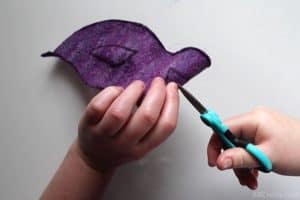 using tiny scissors to cut a slit into a purple wool mask that's folded over
