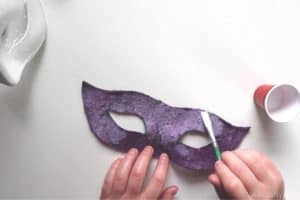 using a paint brush to pant the back of a wet felted carnival mask with Aleene's Fabric Stiffener Draping Liquid