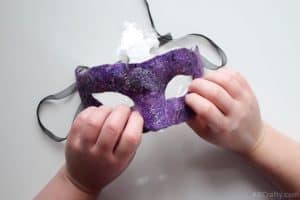 pressing the shaped purple wool carnival mask onto a white plastic mask wrapped in plastic