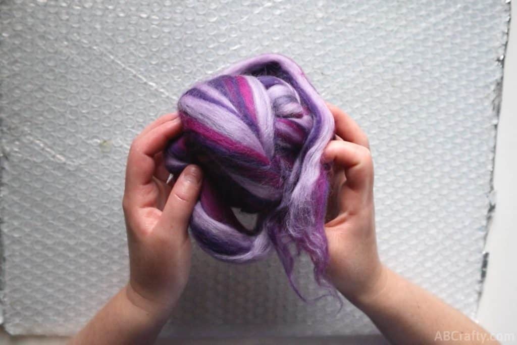 holding a ball of purple and pink wool roving