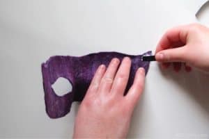 adding a black satin ribbon to the side of the back of a purple handmade carnival mask