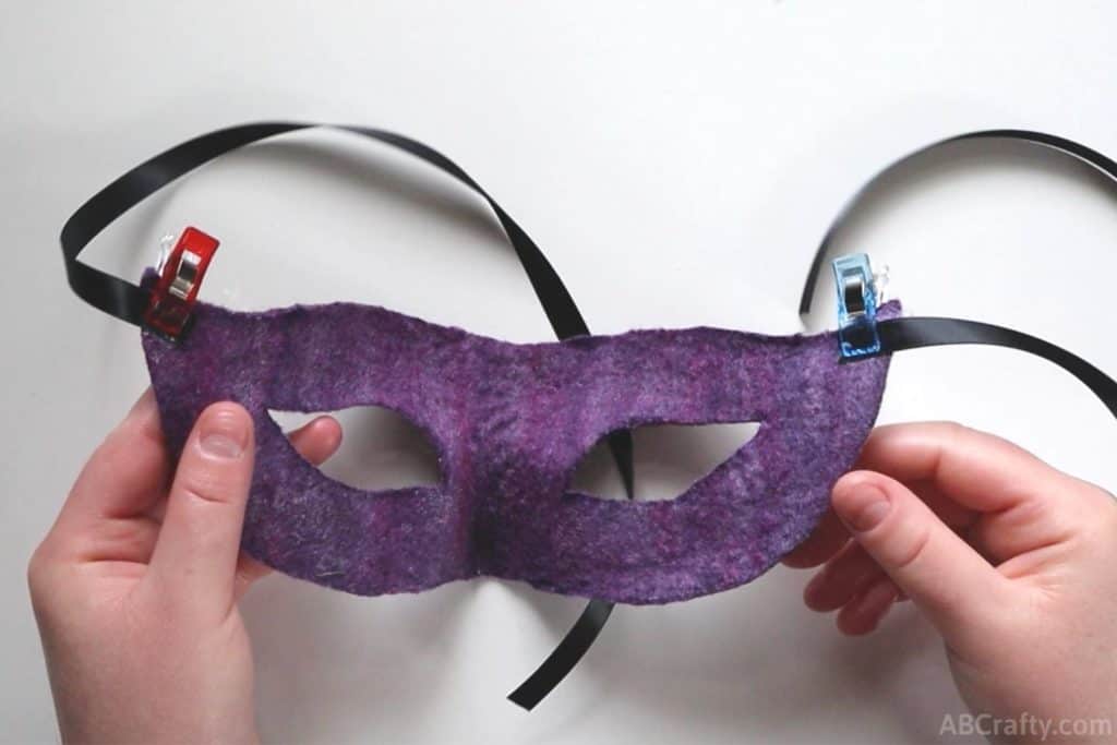 clips holding satin ribbon to the sides of handmade purple masquerade mask