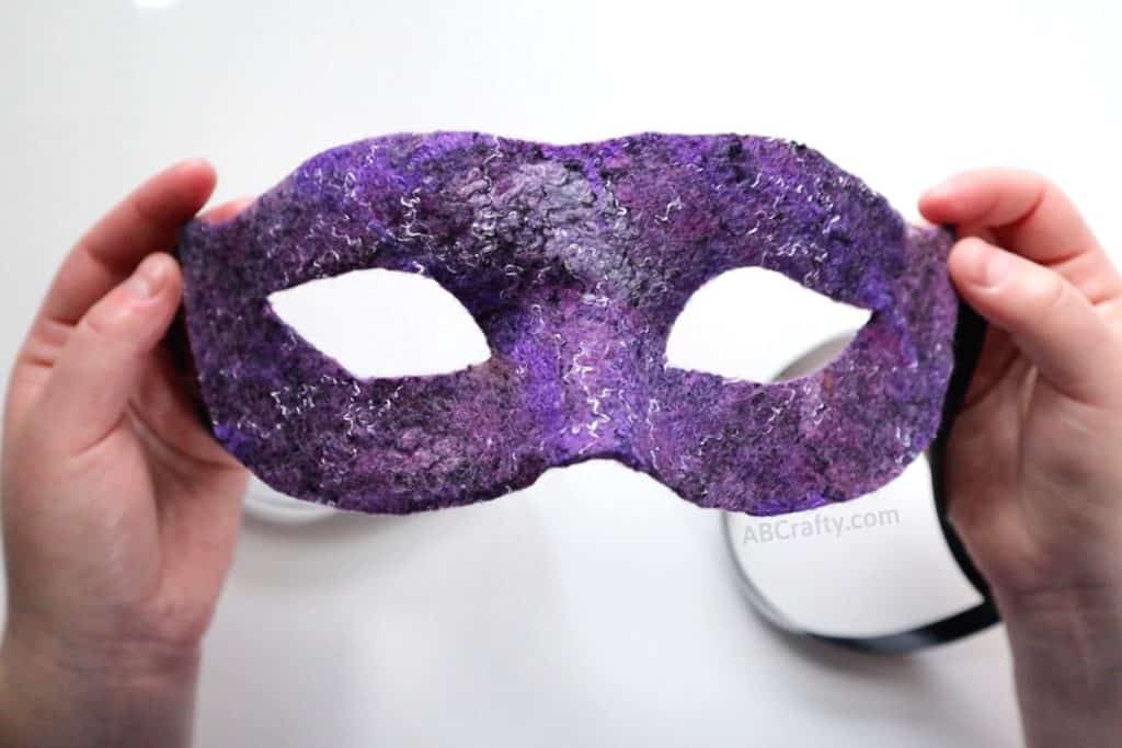 holding the finished handmade purple wet felted Venetian mask