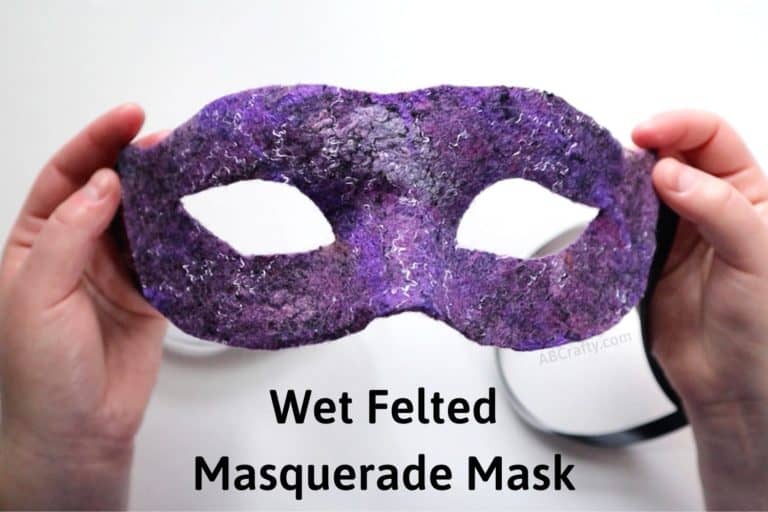 holding a purple silver and black Venetian mask with the title 'wet felted masquerade mask'