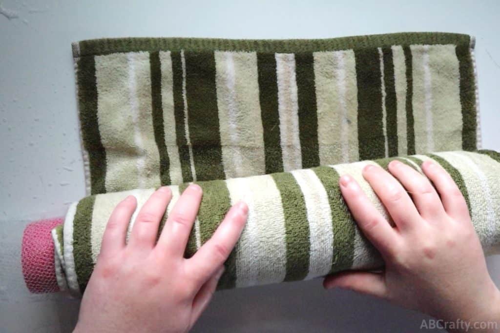 rolling a pool noodle wrapped in a green towel