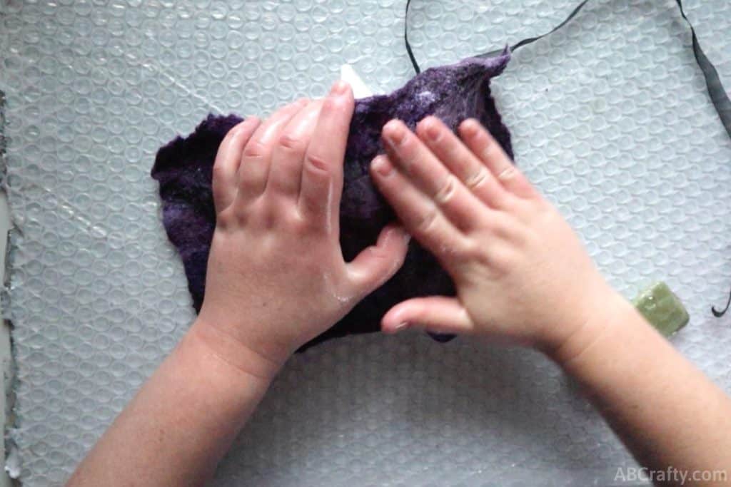 using hands to rub partially felted purple wool on top of a plastic mask