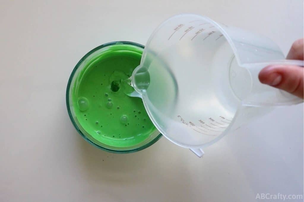 pouring clear slime activator into a bowl of green liquid made of glue